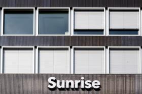 Immagine di uno stabile a listelli dei legno scuro con griglia di finestre dalla cornice bianca e insegna Sunrise