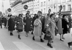Immagine in bianco e nero di donne in cappotto che sfilano reggendo cartelli circolari con la scritta BV4
