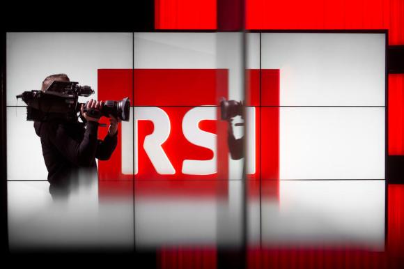 Interno di uno studio televisivo, con grande schermo riportante il logo RSI e un cameraman di profilo