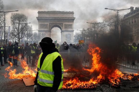 Incendio nelle strade di Parigi. Un gilet giallo con il viso nascosto e dietro l arco di trionfo. e ovunque fiamme