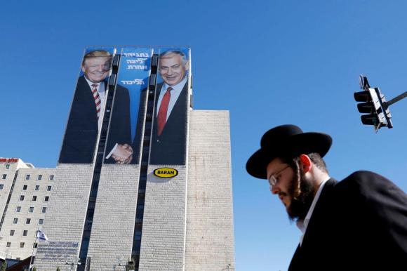 Un ebreo ortodosso mentre cammina a Gerusalemme e dietro di lui in una gigantografia Netanyahu dà la mano a Trump