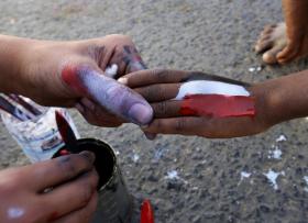 Immagine della mano di un adulto che regge quella di un bambino, sulla quale è dipinta una bandiera yemenita