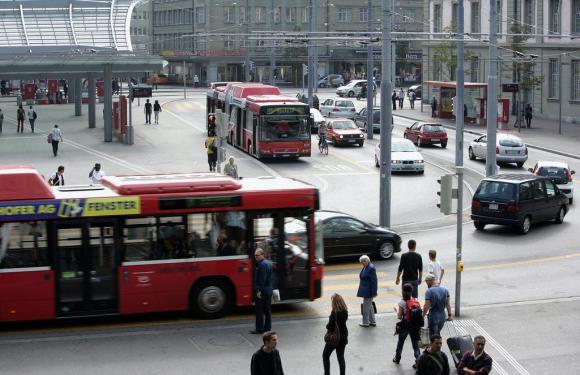 La piazza antistante la stazione ferroviaria di Berna: si vedono due bus cittadini, diverse auto e tanta gente