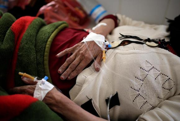 Primo piano di mani di donna anziana appoggiate in prossimità della vita con flebo attaccate, su letto d ospedale