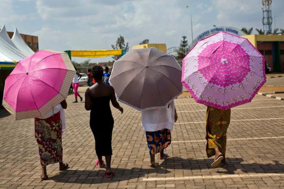 Quattro donne con abiti colorati e ombrelli parasole riprese di schiena mentre camminano in una piazza