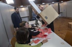 Un urna elettorale viene svuotata su un tavolo alla presenza di diverse persone: le schede rosse invadono il tavolo