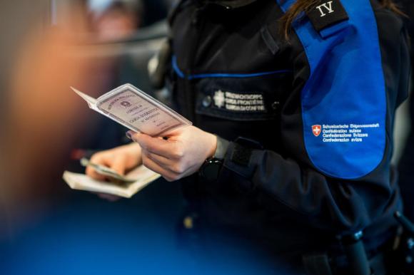 Primissimo piano di una guardia di confine svizzera in uniforme che controlla una carta d identità italiana