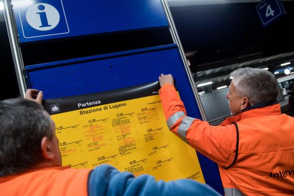 Due operai delle ferrovie stanno cambiando il tabellone don l orario dei treni nella stazione di Lugano
