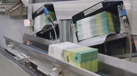 Mazzette di banconote da 50 franchi passano attraverso una macchina industriale (che verosimilmente le confeziona)