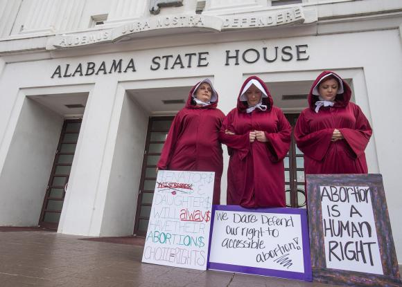 tre donne con dei cartelli davanti alla sede del parlamento dell Alabama