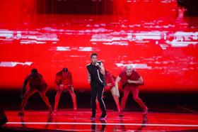 Luca Hänni su un palco con scenografia completamente rossa e tre ballerini di rosso vestiti