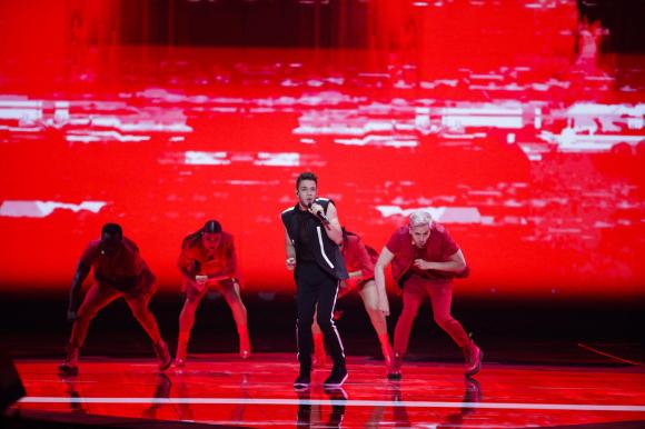 Luca Hänni su un palco con scenografia completamente rossa e tre ballerini di rosso vestiti