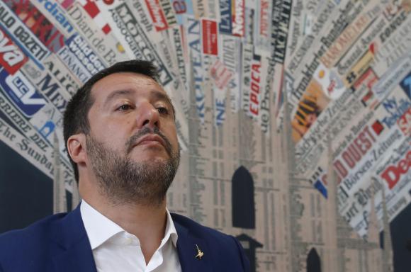 Primo piano di Matteo Salvini nella sala stampa estera; dietro di lui, decorazione realizzata con decine di testate di giornale