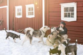 Frau mit Hunden vor rotem Holzhaus im Schnee