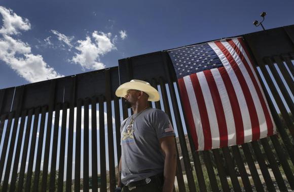 La barriera tra Messico e Stati Uniti con appeso una bandiera americana e davanti un uomo di colore