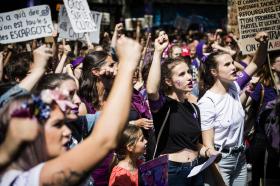 Gruppo di manifestanti donne in una piazza; molte indossano qualcosa di viola; palloncini e bandiere viole