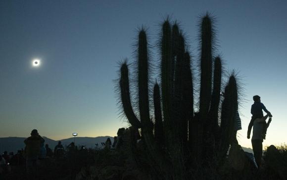 Cactus e persone con strumenti oculari, visti in controluce durante un eclissi totale di sole.