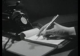 Una mano prende appunti su un bloc notes appoggiato su una scrivania accanto a un apparecchio telefonico d epoca
