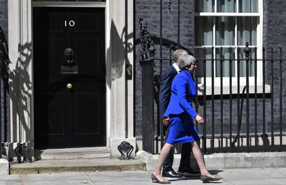 Theresa May. vestita coloro blu cobalto, lascia il 10 di Downing Street accompagnata dal marito.
