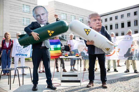 Due persone con le maschere di Putin e Trump con in mano ciascuno una bomba atomica