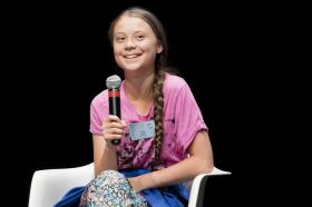Greta Thunberg sorridente, seduta con un microfono in mano al vertice Smile for future