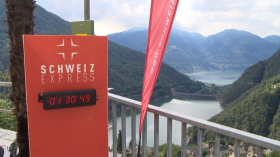 Vista dall alto di un bacino lacustre circondato da montagne, con totem con scritta Schweiz express e cronometro