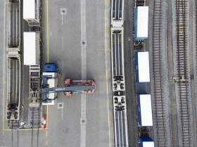 Vista dall alto di binari ferroviari e di una gru che sposta container da motrici stradali a vagoni