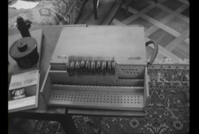 Immagine di un apparecchio che ricorda solo sommariamente una macchina da scrivere, accanto a un tavolino