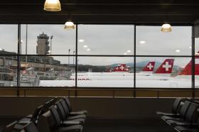Aerei con livrea rossocrociata parcheggiati in parallelo, visti attraverso le finestre di un aeroporto