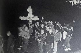 gente che fa il saluto nazista di fronte a una croce in fiamme