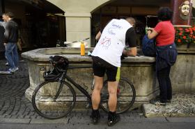 Un ciclista (che indossa maglietta con illustrazione che mostra il percorso da Ginevra a Berna) si rinfresca a una fontana