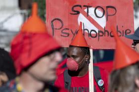 Persone manifestano con un imbuto in testa a mo di cappello e cartello Stop psychophobie