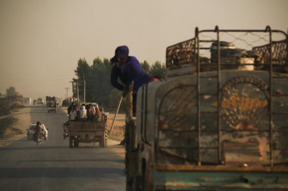 Strada extra urbana fotografata al crepuscolo; si vedono dei camioncini, alcuni -in lontananza- carichi di civili