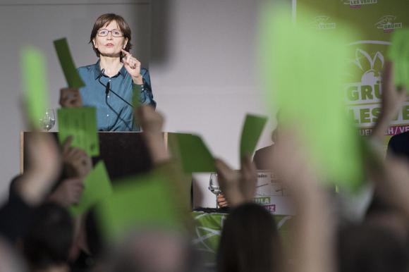 Donna su un podio e mani alzate che mostrano delle schede verdi.