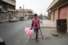 Boy in pink t-shirt stands on crutches with bags of cotton candy in his one hand