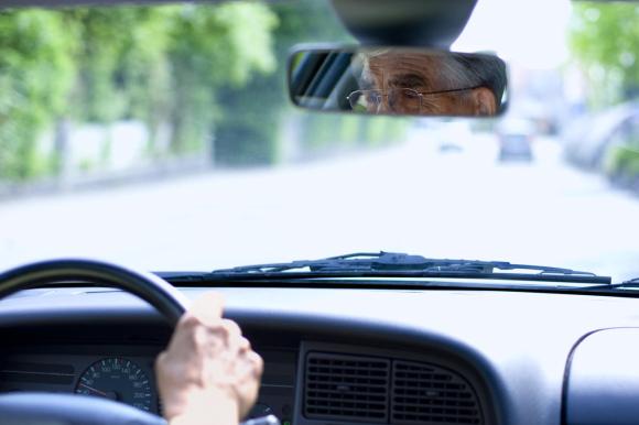 Un anziani al volante della sua auto: lo si vede dallo specchietto retrovisore