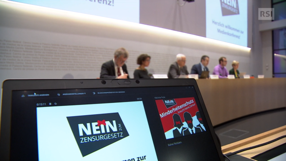 Sei persone sedute al tavolo di una sala stampa; in primo piano, un logo Nein Zensurgesetz