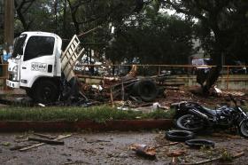 Un camioncino parcheggiato e una moto, a terra, lungo un viale alberato; danneggiati da frammenti di un esplosione