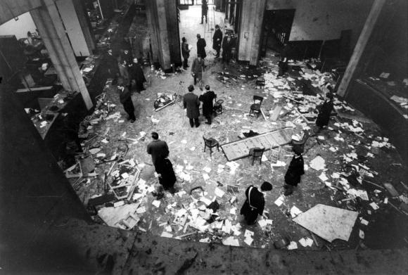 Foto b/n. Vista dall alto dell atrio di un edificio bancario, con carte e detriti su tutto il pavimento; poche persone