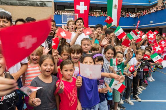 folla di bambini che sventolano bandierine svizzere e messicane.