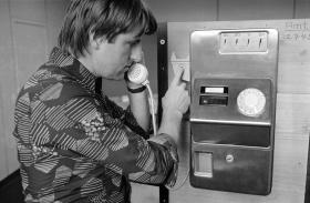 Un uomo con camicia stampata preme il tasto per riattaccare mentre regge la cornetta di un telefono pubblico