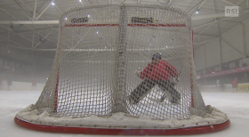 Porta di hockey su ghiaccio vista da dietro; portiere accovacciato mentre attaccante si allontana