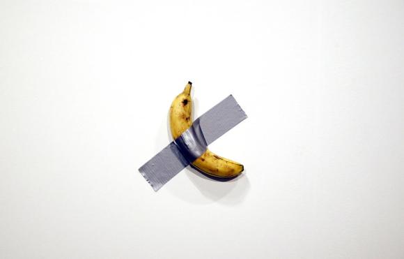 Installazione di Cattalan; una banana vera appesa a un muro con del nastro adesivo grigio.