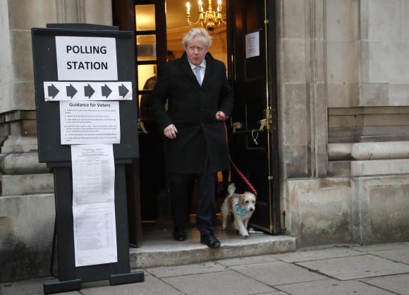Boris Johnson mentre esce dal seggio elettorale con un cagnolina al guinzaglio.
