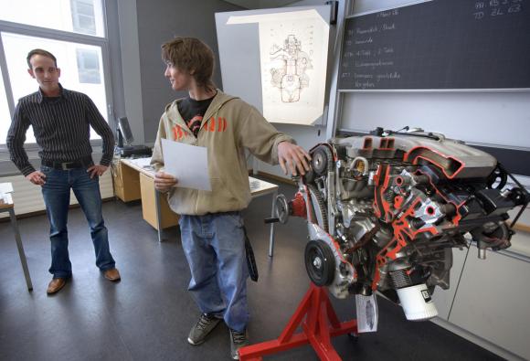 Un apprendista meccanico a scuola con un docente e un motore.