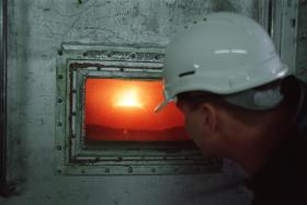 Un operaio che indossa un casco grigio, di spalle, osserva l interno di un forno industriale attraverso la finestrella