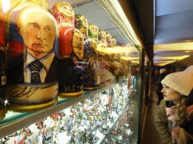 Vetrina colma di souvenir in negozio pieno di luci. In primo piano matrioske con dipinti Putin e Stalin. Una cliente guarda
