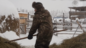 Un uomo sposta del fieno in una fattoria dove tutto è coperto da una coltre di neve
