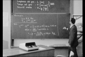 Immagine b/n di un maestro che spiega formule matematiche alla lavagna.