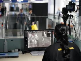 una funzionaria guarda un monitor in cui si vedono dei passeggeri in aeroporto